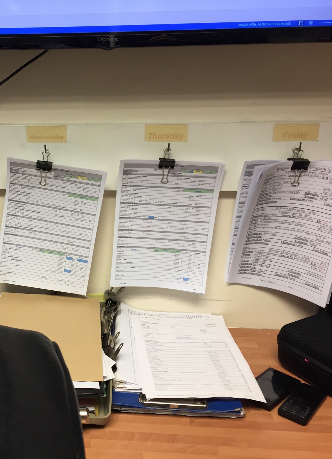 Funeral documents hung behind a desk, clipped together and arranged in order of funeral date