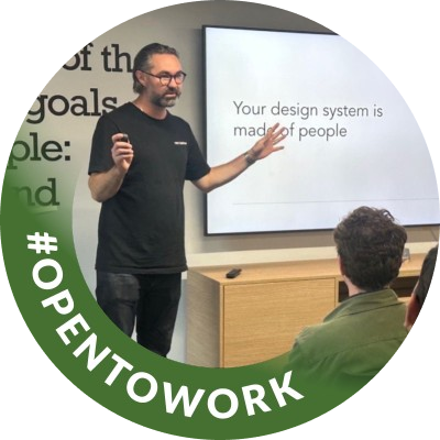 Matt speaking at an event in front of a slide reading ‘Your design system is made of people’, with an Open To Work badge